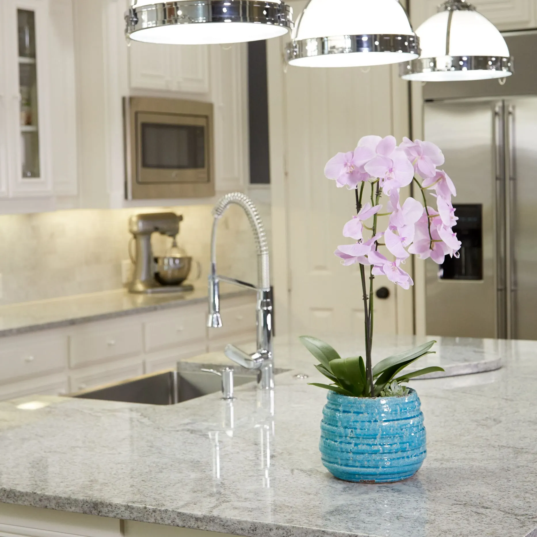 Light gray and white granite island with a pink orchid in a blue pot, in a kitchen with white cabinets
