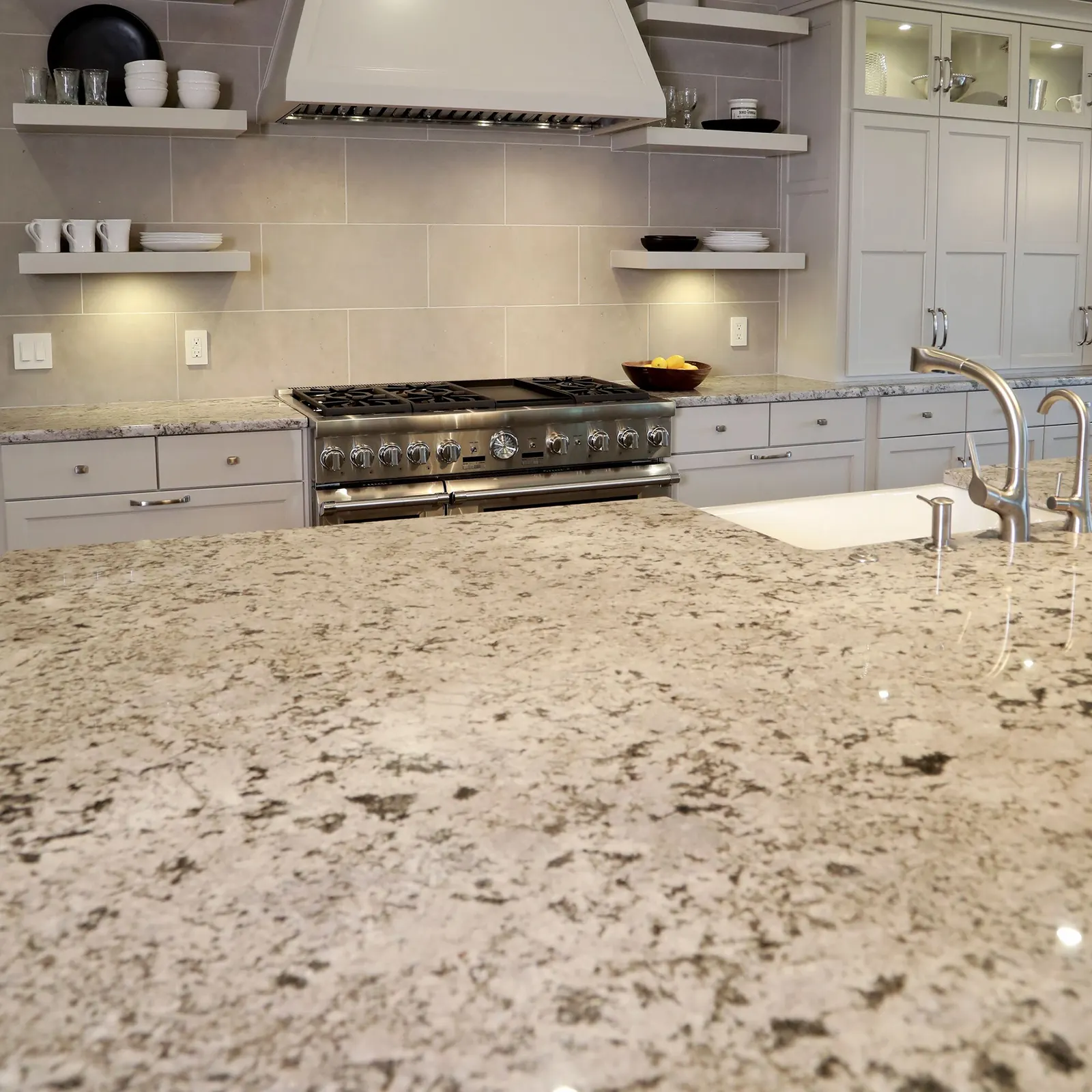 Close view of a polished granite island with a busy cream, gray and brown speckled pattern, a range behind it