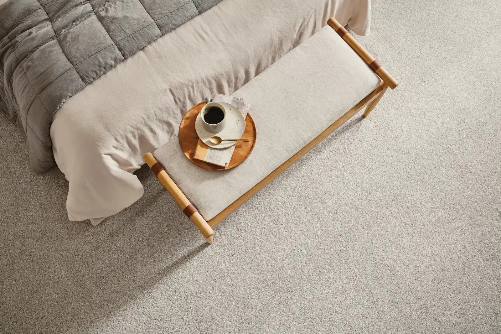 Soft beige carpet seen from above at the foot of a bed with an upholstered bench and a coffee tray