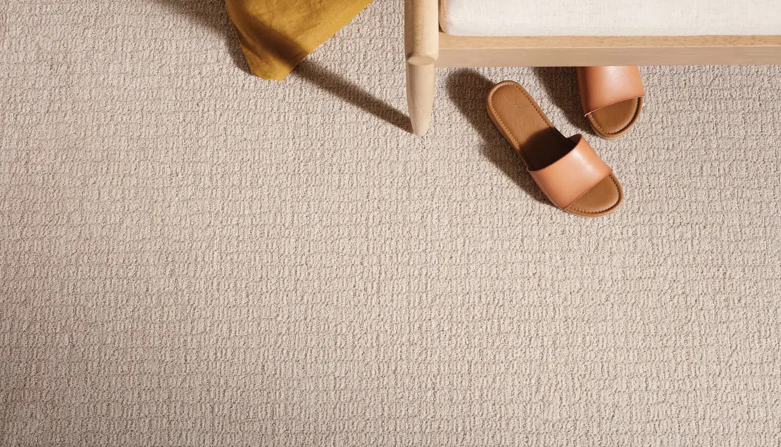 Close view of beige patterned loop carpet beside a bench leg and a pair of leather sandals