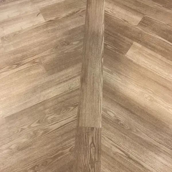 Close-up of light-brown wood-grain luxury vinyl plank, with one loose plank laid across the installed field.