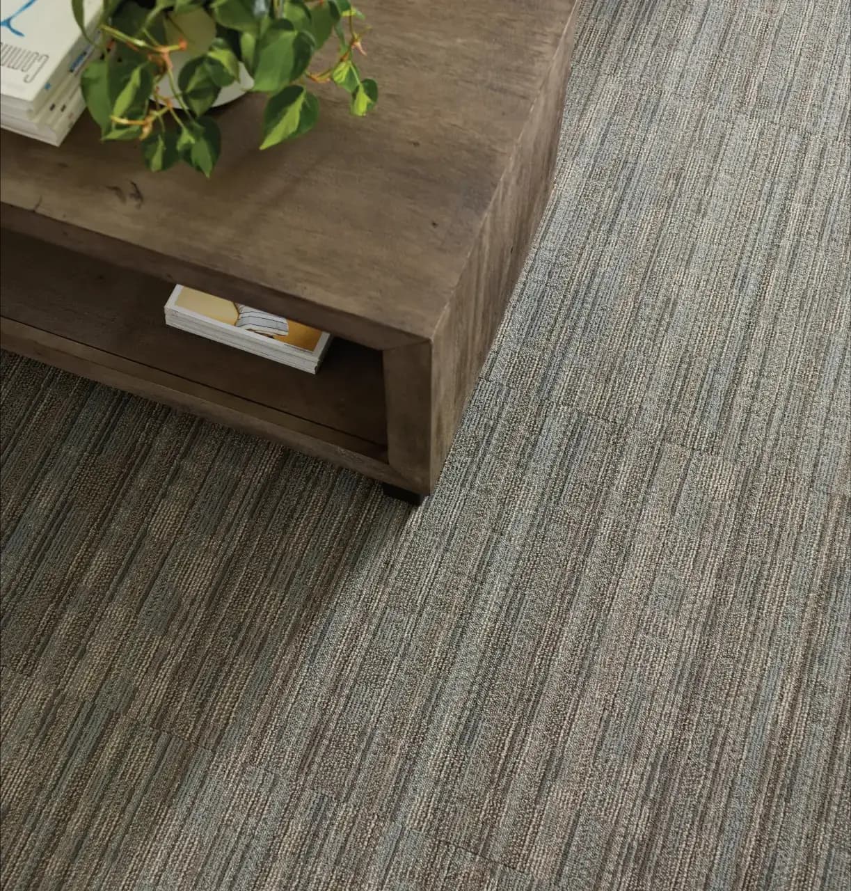 Close-up of textured commercial carpet tile in mixed browns and grays under a wooden coffee table