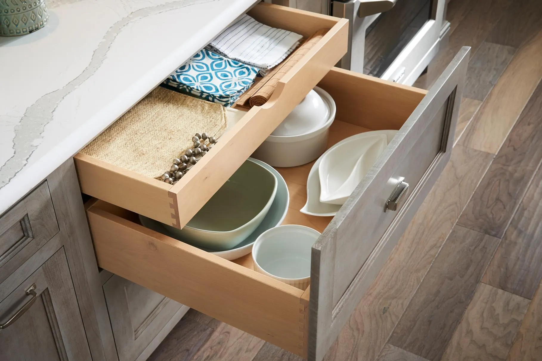 Open deep kitchen drawer holding bowls and serving dishes, with a shallow inner drawer of linens above