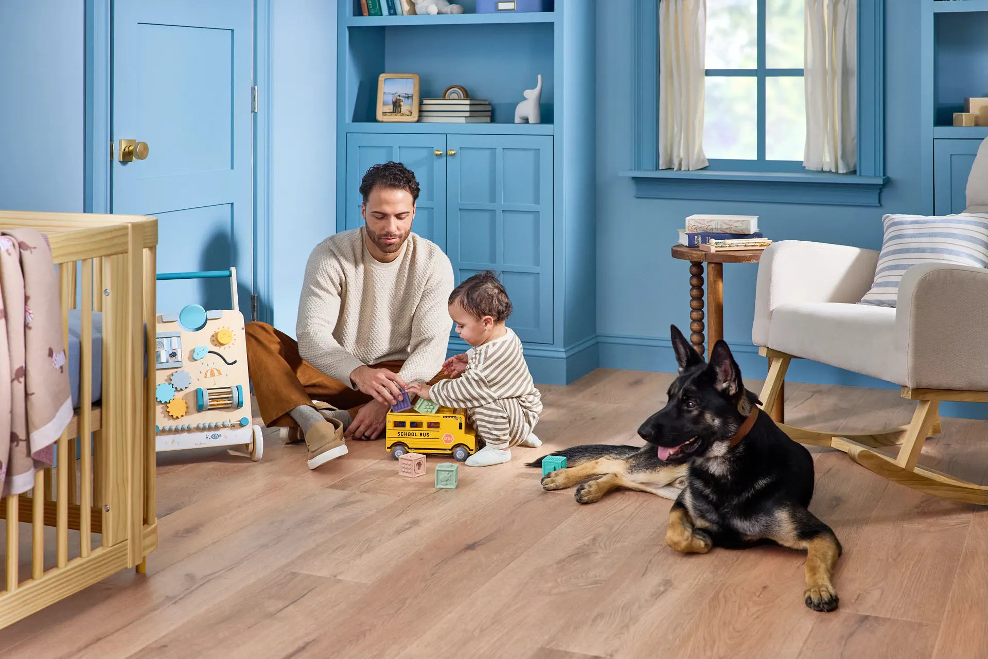 A dad and toddler playing on COREtec Sand Dollar Oak vinyl plank flooring while the family dog lies nearby, a line we carry