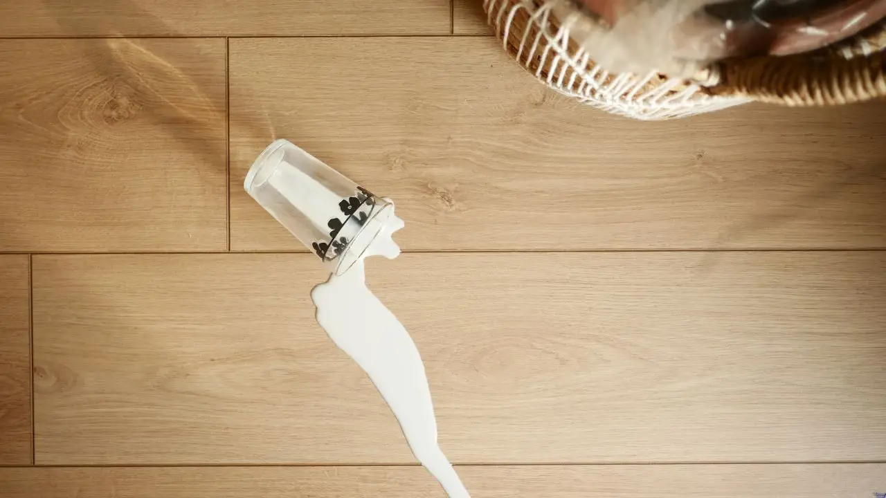 Glass of milk spilled on a wide-plank light oak floor, showing the importance of spill-resistant durable flooring