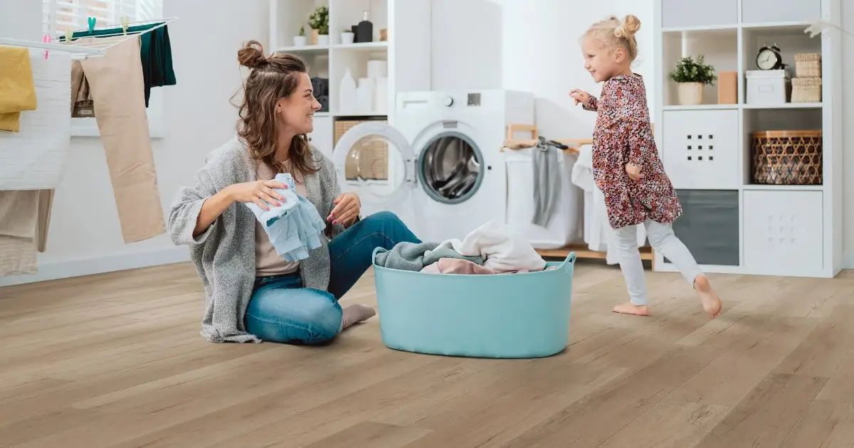 Mother and young daughter doing laundry on light blonde wood-look luxury vinyl plank flooring in a bright family laundry room