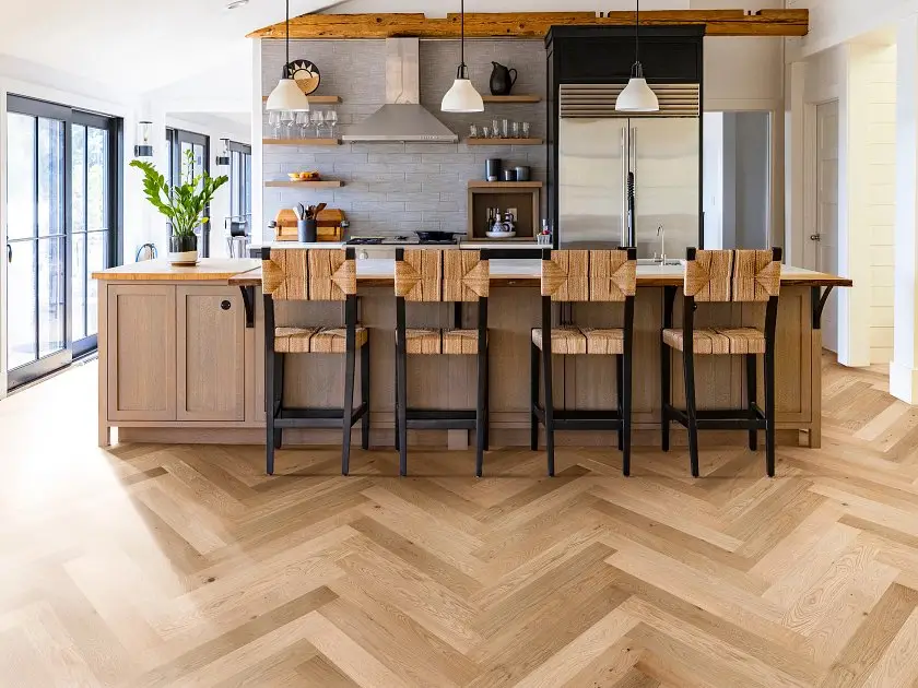 Herringbone-pattern wide-plank hardwood flooring in a modern kitchen with island and bar stools
