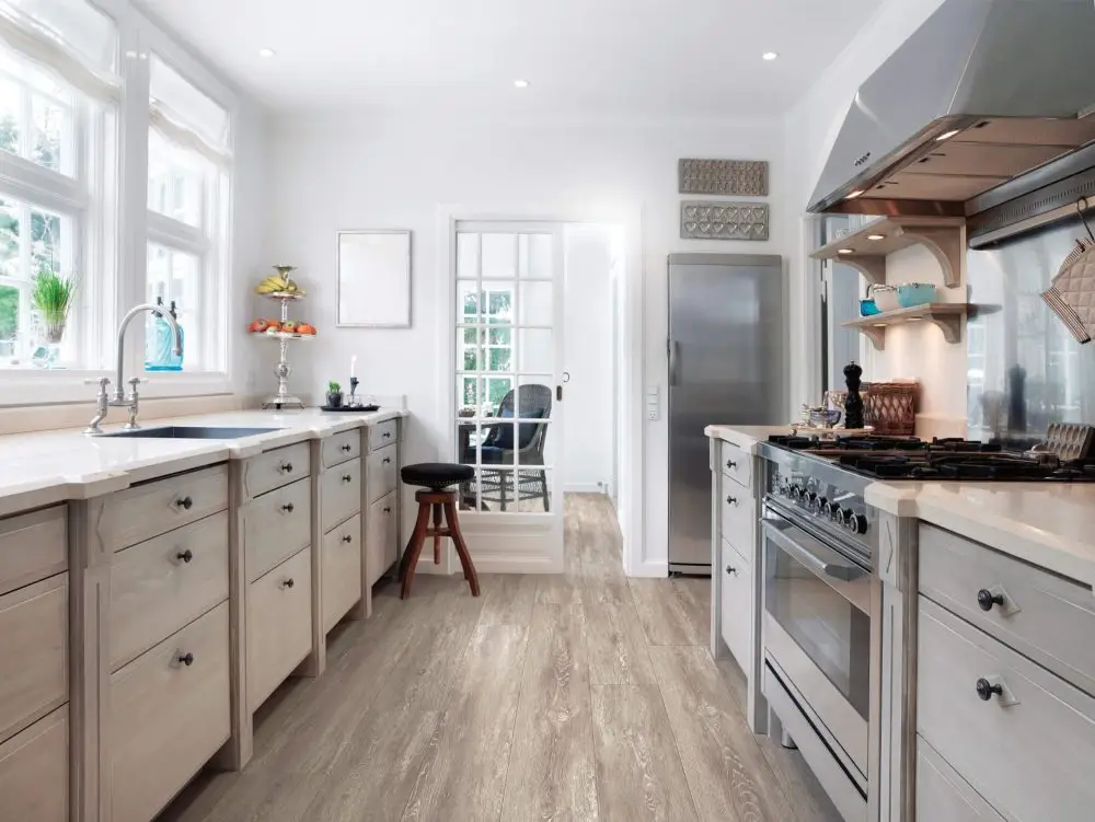Light gray wood-look plank flooring in a bright kitchen with white cabinets and stainless steel appliances