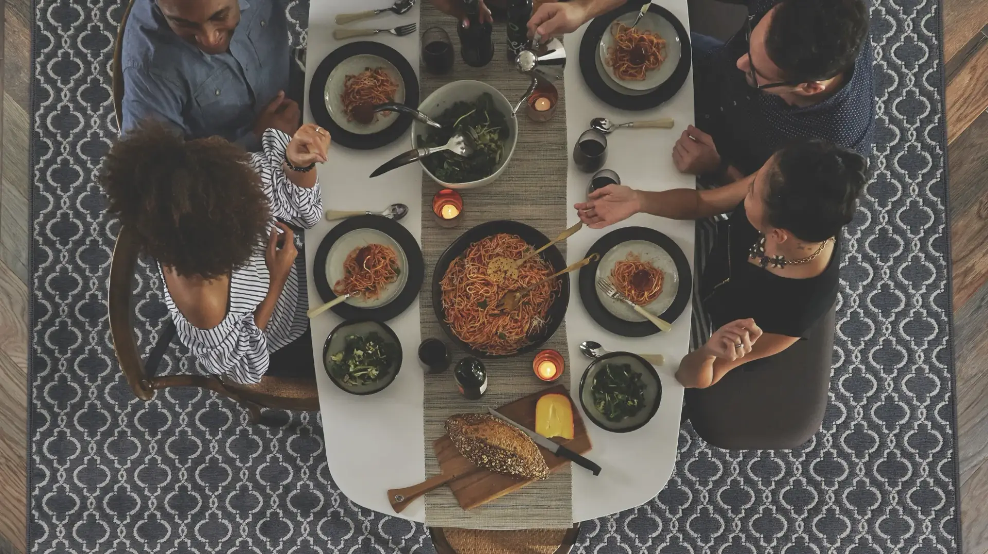 Overhead view of friends gathered around a dinner table on hardwood flooring with a patterned area rug