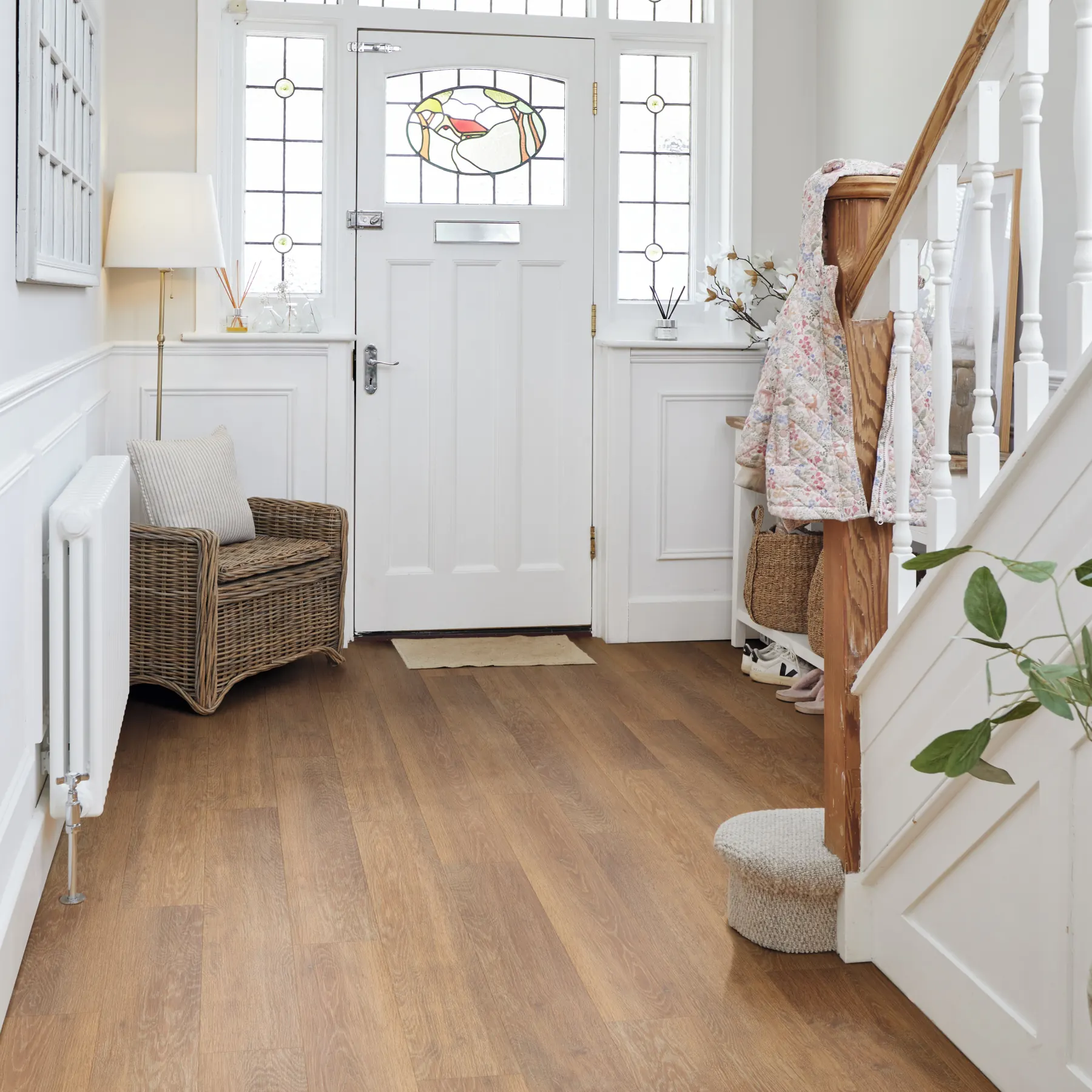 Finished oak-look plank floor meeting white painted baseboards and wall paneling in an entry hall