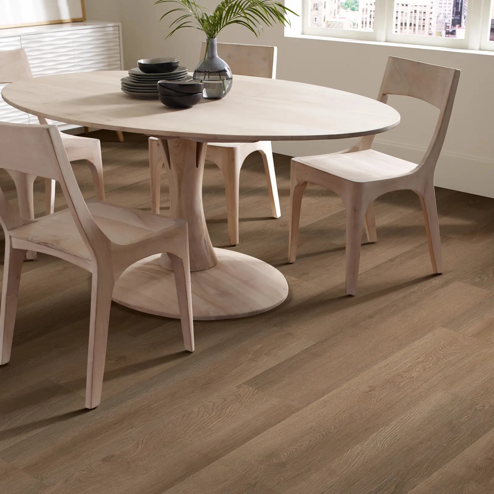 Wood-look vinyl plank floor meeting a white baseboard below a window, with a pale wood dining set