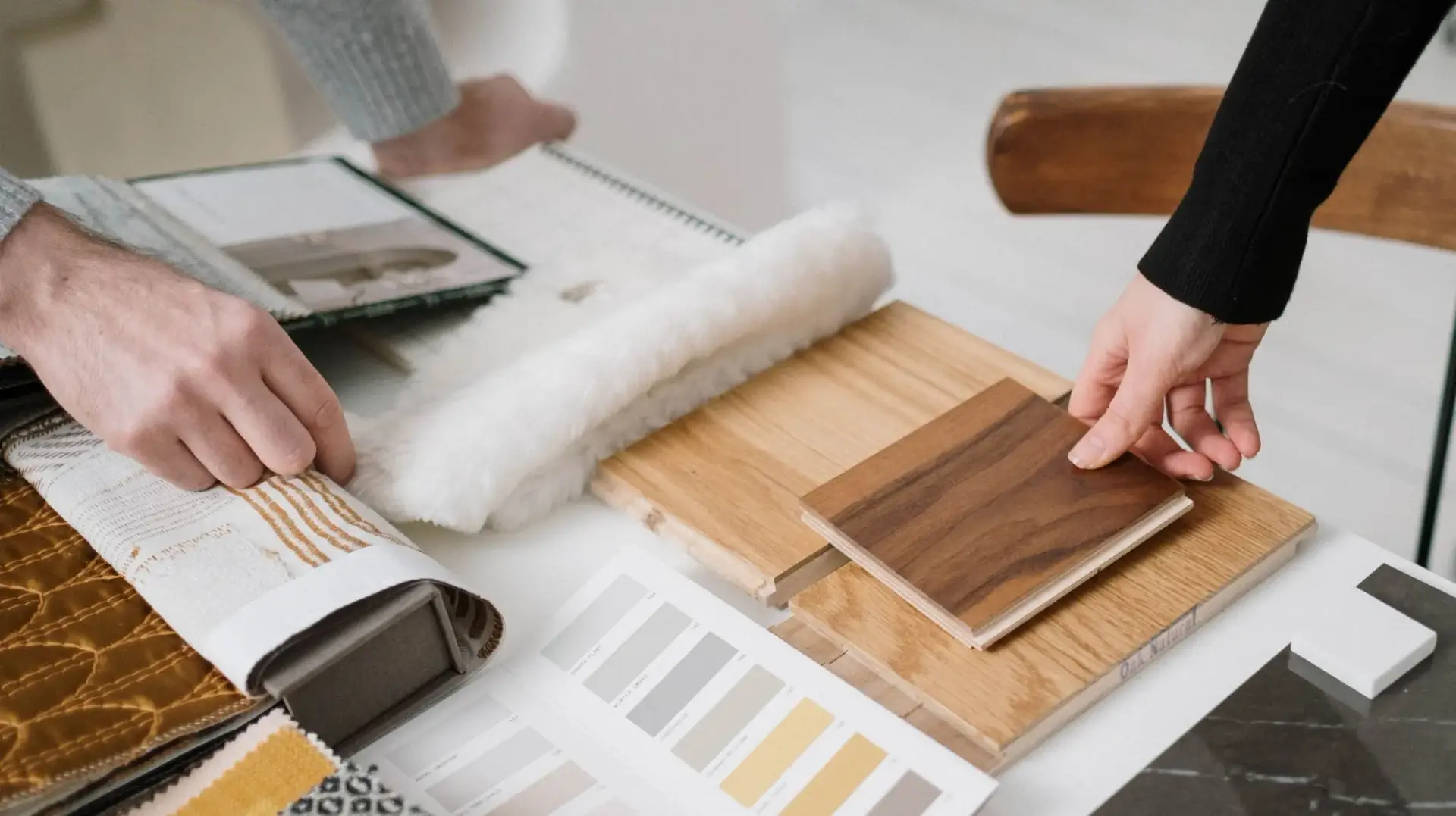 Two customers comparing fabric swatches, paint chips, and hardwood floor samples at a flooring showroom