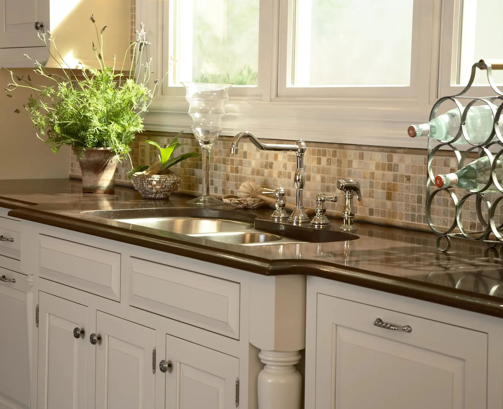 Cream cabinet doors with round knobs beside a drawer with a bar pull, under a dark countertop and sink