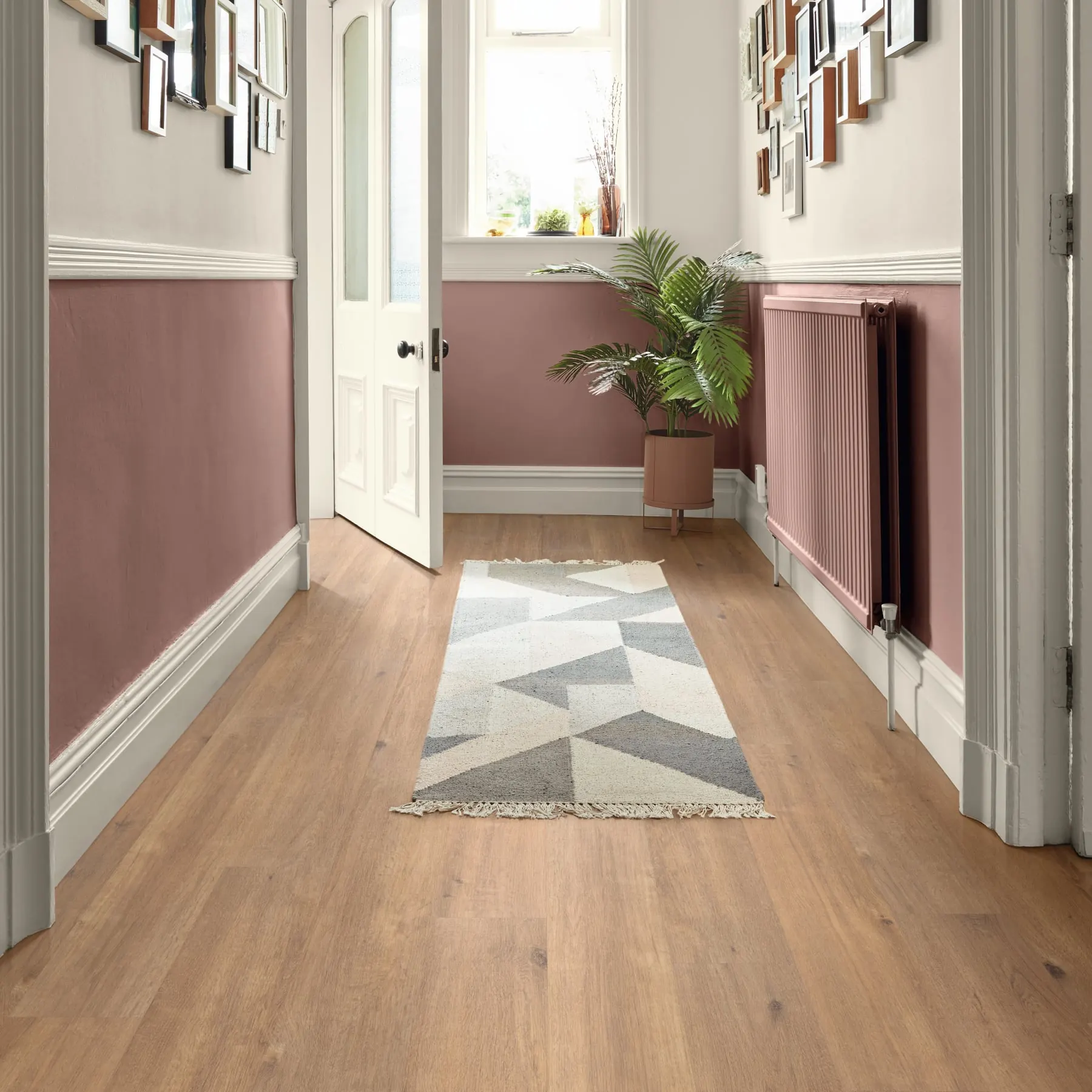 Oak-look vinyl planks running the length of a narrow hallway toward a window, with a runner rug