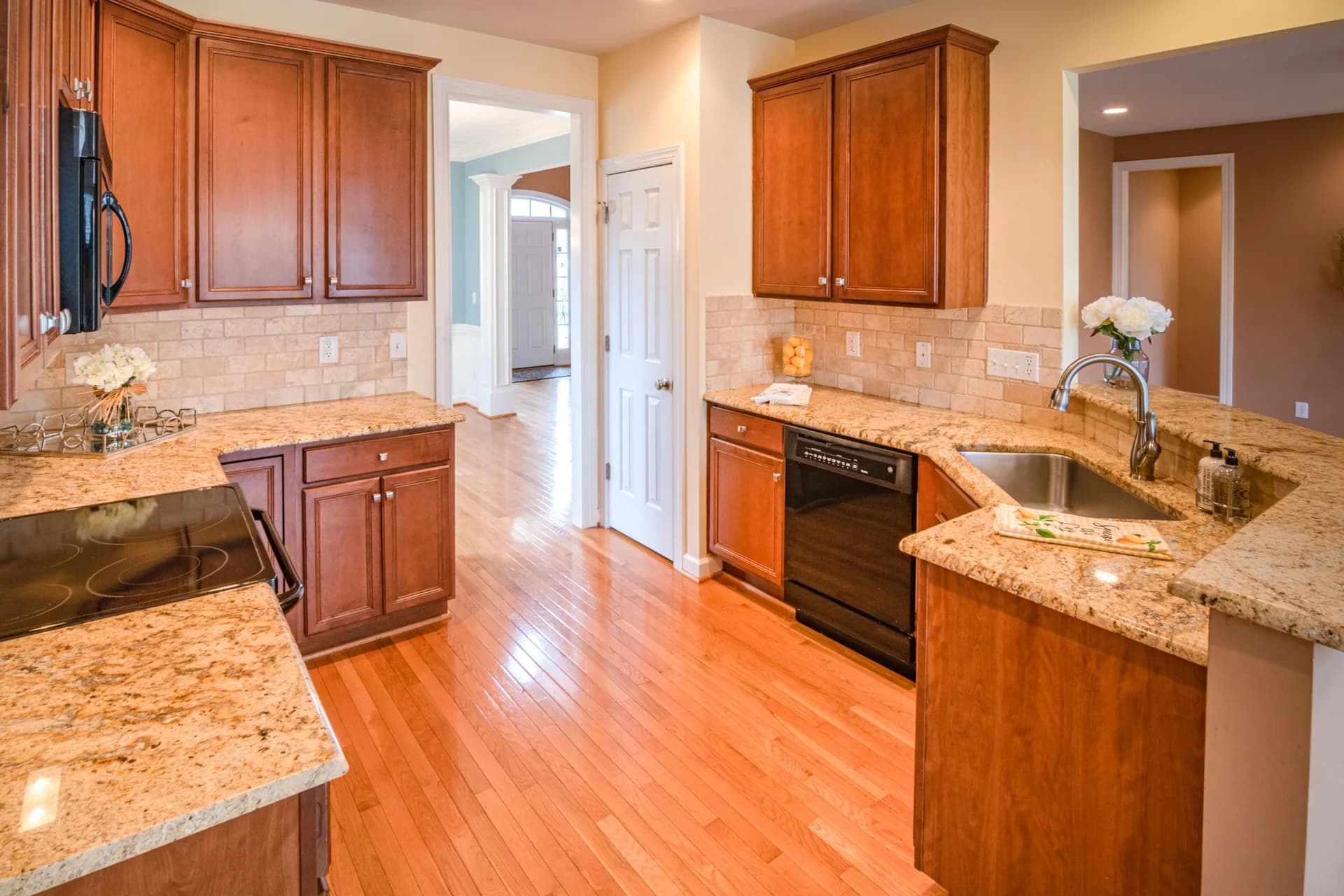 Cream and gold speckled granite countertops in a galley kitchen with reddish brown wood cabinets and a stone tile backsplash.