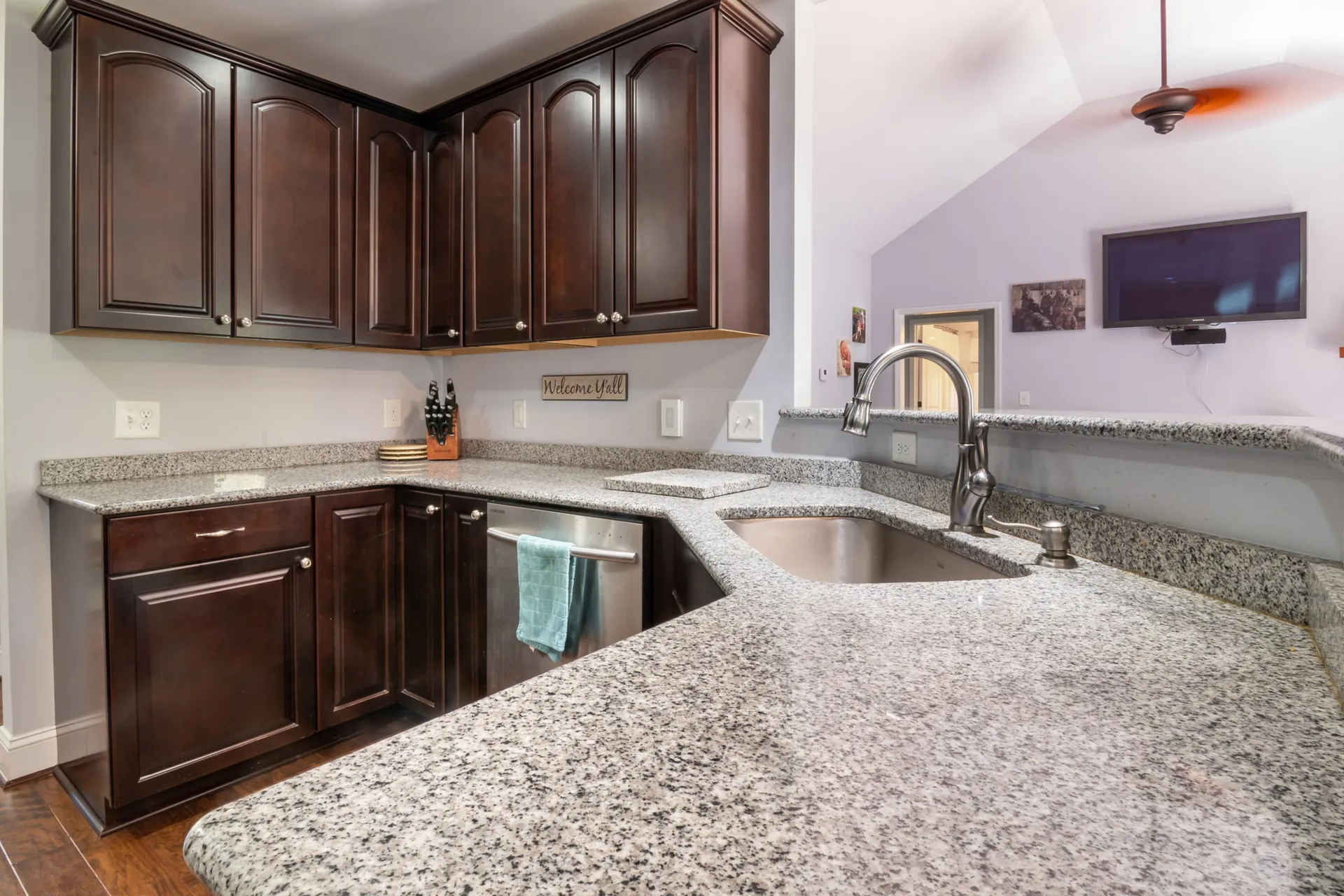 Speckled gray and white granite countertop wraps a kitchen corner into a raised bar above dark espresso cabinets and an undermount sink.