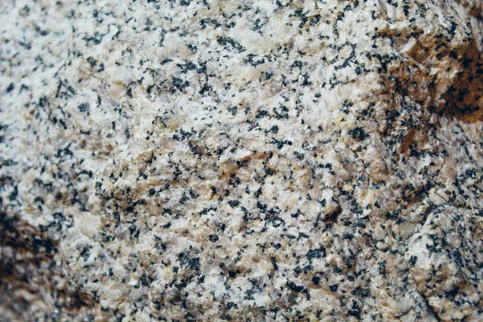 Close-up of natural granite, speckled cream, gray and black with rust brown patches across a rough, unpolished face.