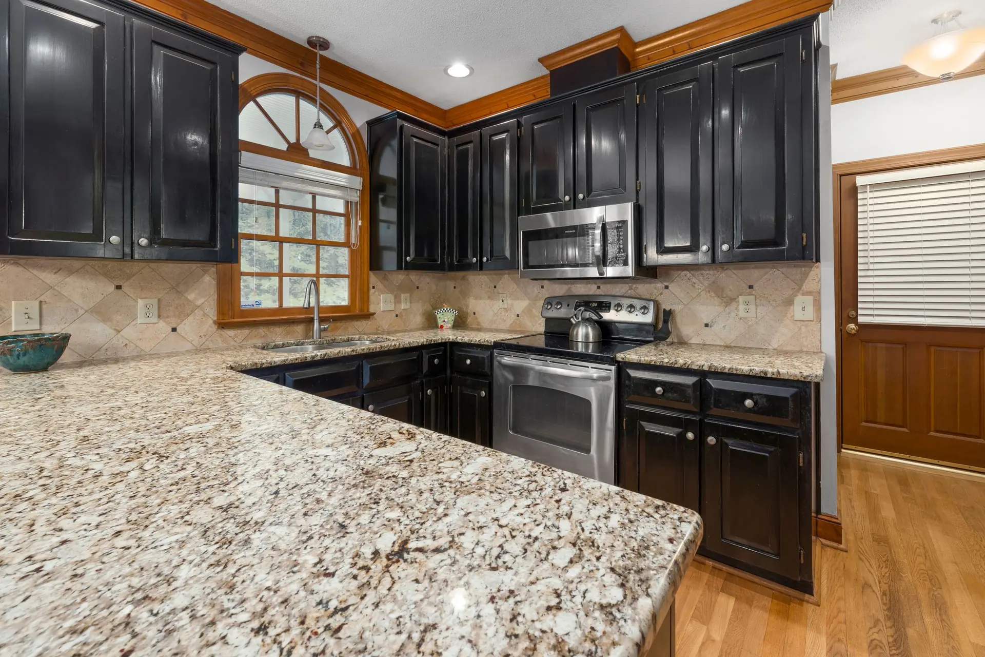 Speckled beige and brown granite countertop on a kitchen peninsula, with black cabinets and a tile backsplash behind the range.