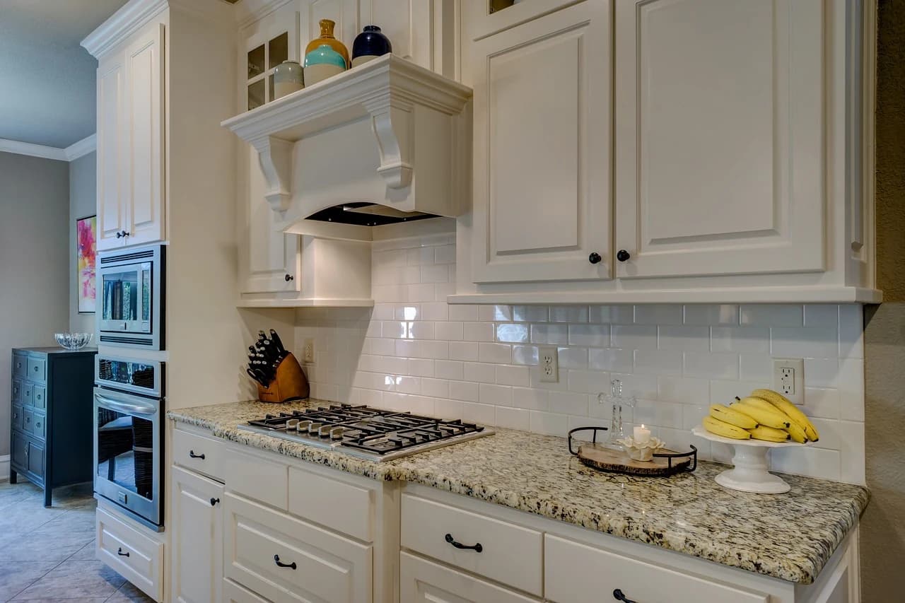 Speckled beige granite countertop in a kitchen with cream raised panel cabinets and a white subway tile backsplash.