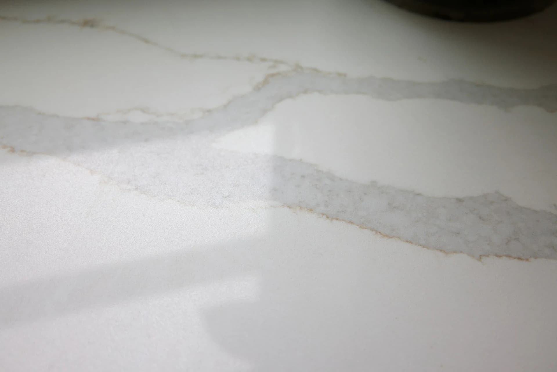 Close-up of a polished white quartz countertop with soft gray and gold veining running across the surface.