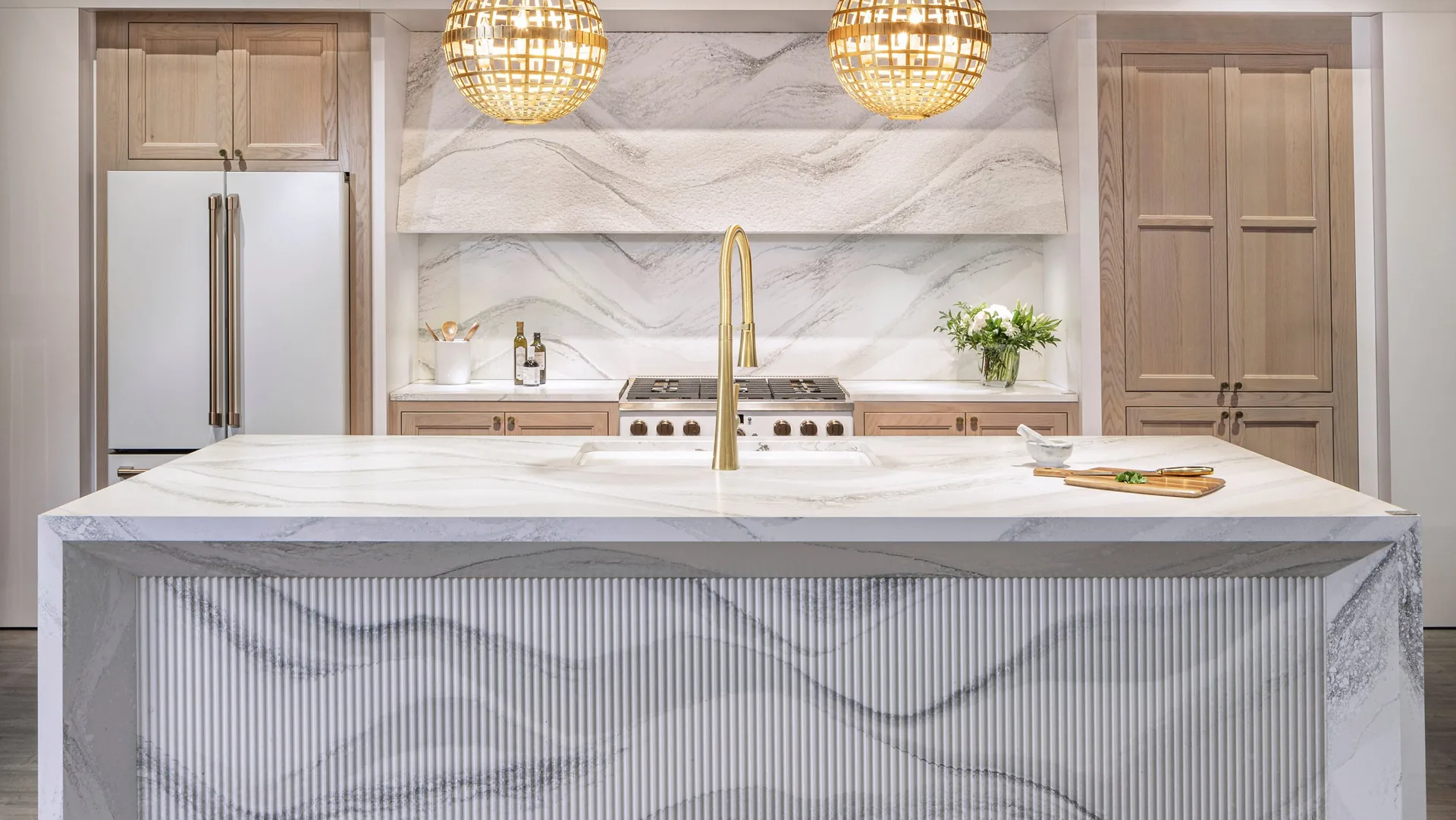 Cambria Harlow quartz slab backsplash and island in a white and wood kitchen, from the Cambria line we carry