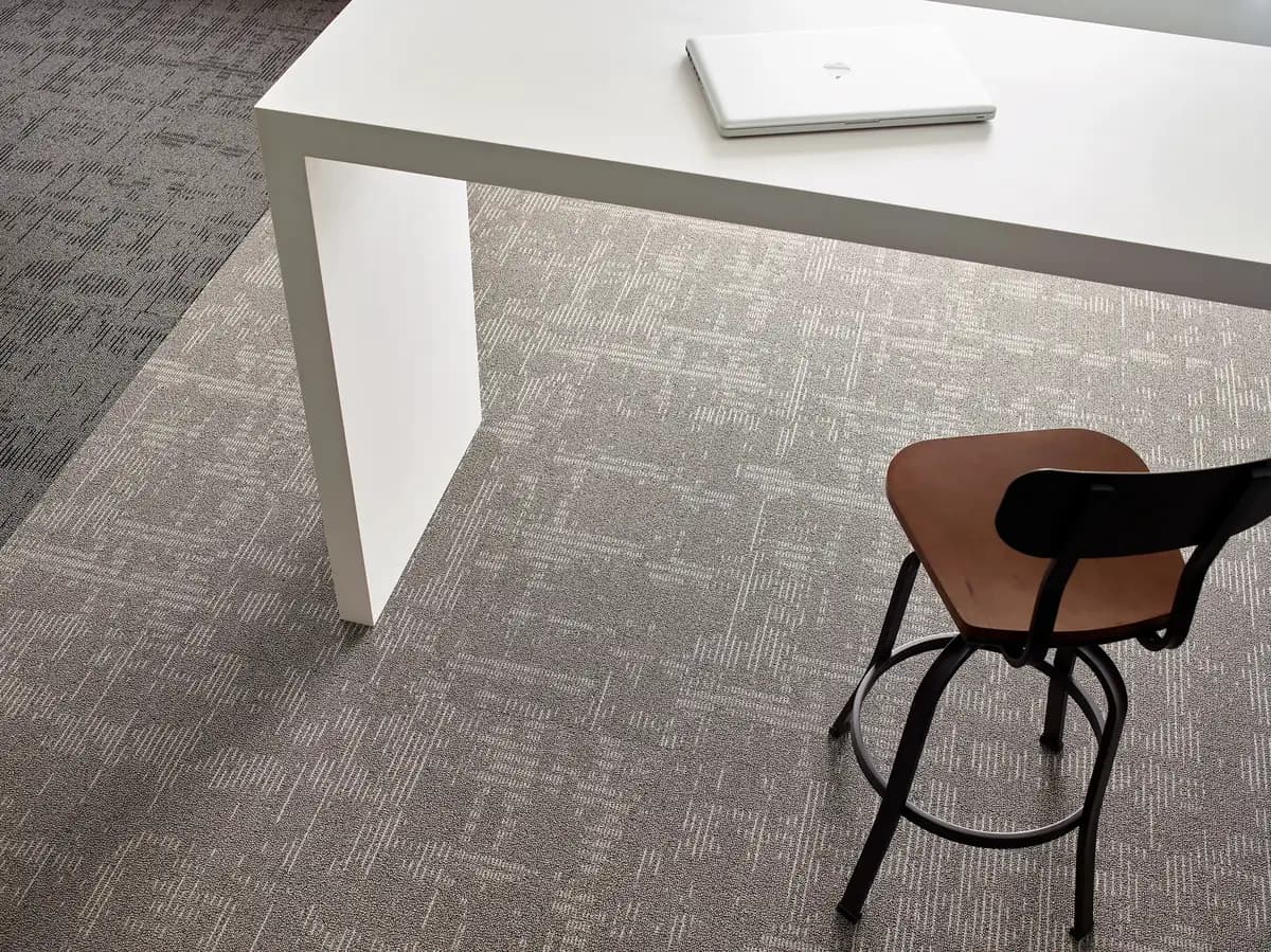Gray patterned Philadelphia Commercial carpet tile in an office workspace with a white table and a wood stool.