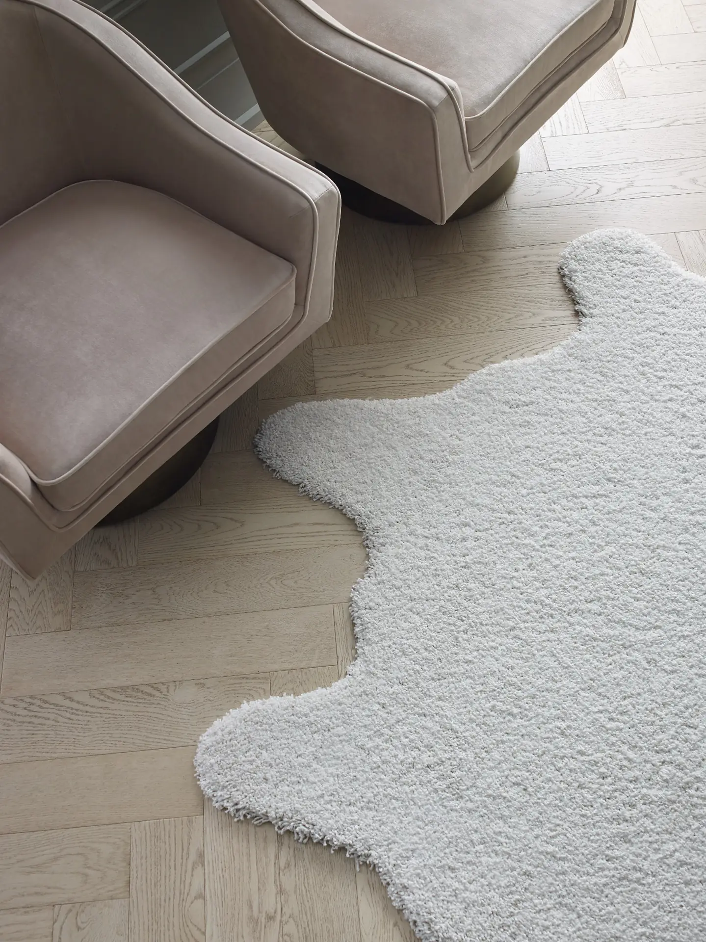 Shaw Floors Fifth Avenue Oak hardwood in Astor, a pale herringbone floor with a white shag area rug and two blush velvet chairs on round bases.