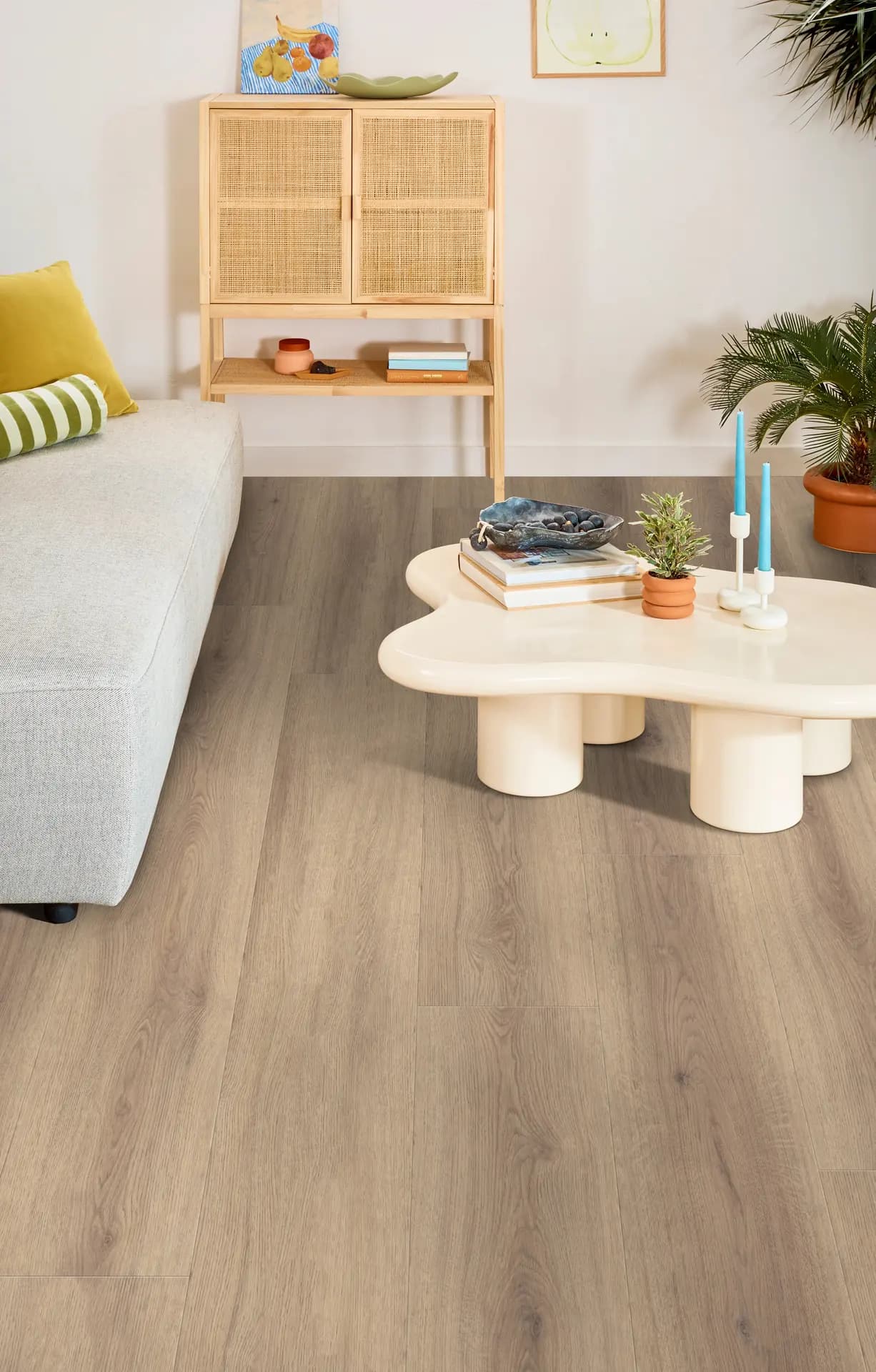 Shaw Floors Briard luxury vinyl plank in Feathered Oak runs across a living room with a gray sofa, rattan cabinet and curvy cream coffee table.