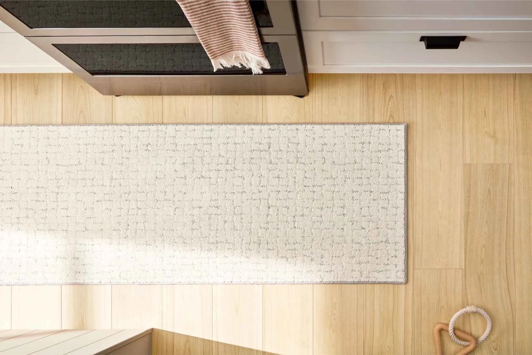 Shaw Floors Cattitude luxury vinyl plank in Hygge, a pale blond wood look, with a bound ivory runner rug in front of a stainless range.