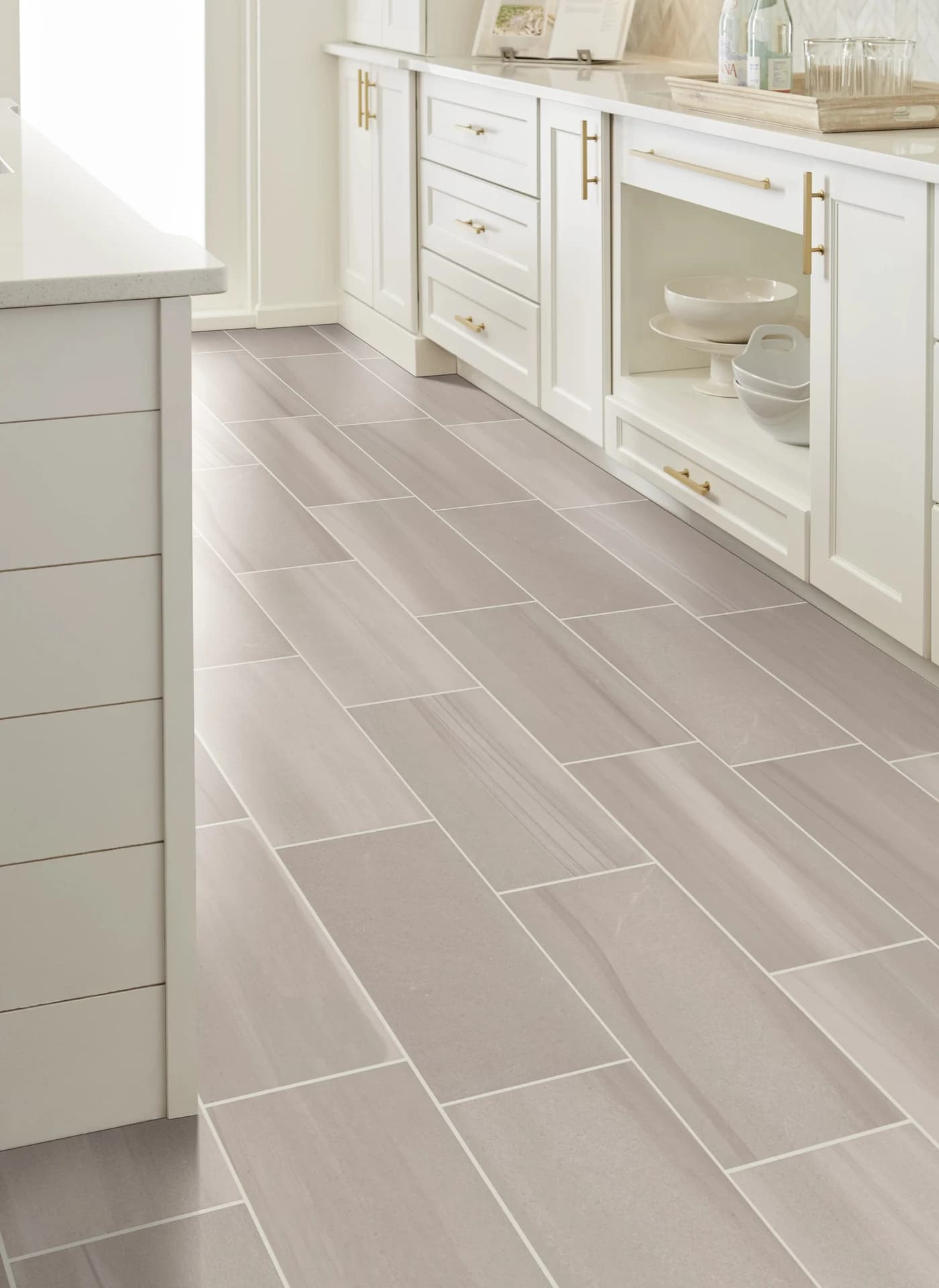 Light gray rectangular floor tile running past white shaker cabinets with brass pulls. Tile flooring for Davenport, FL homes