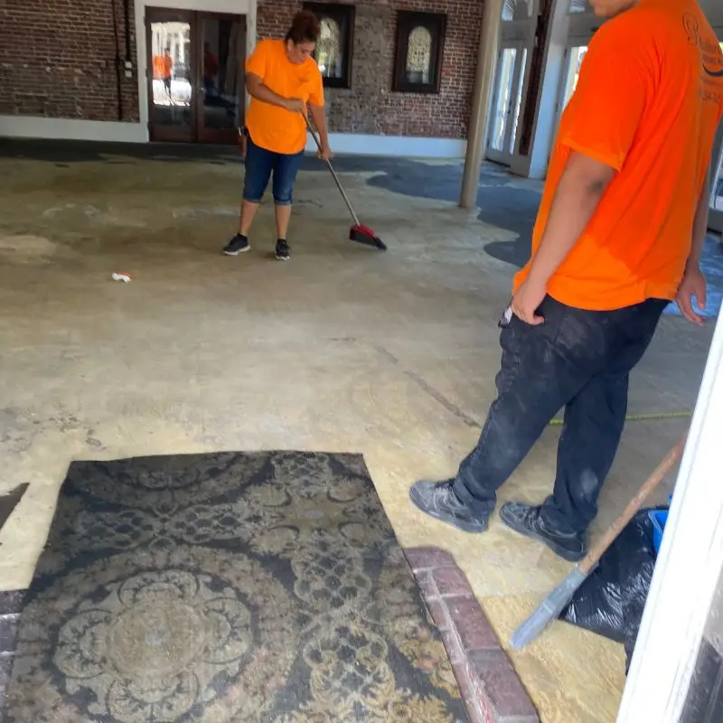 Crew sweeping the prepped concrete subfloor with the old patterned carpet pulled back, ready for the new install