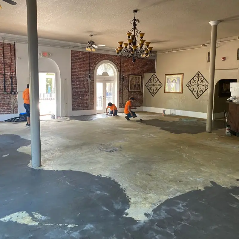 Wide view of the Arabella's Ristorante dining room with exposed brick, chandeliers, and crew prepping the subfloor for new carpet