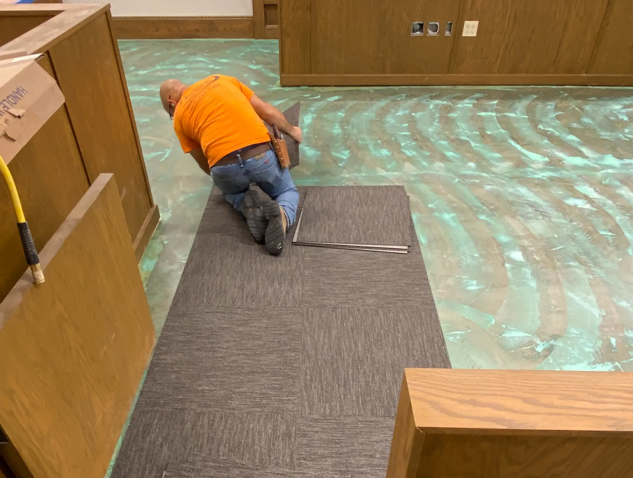 Setting grey carpet tile into troweled adhesive beside the oak bench at the DeSoto County Courthouse