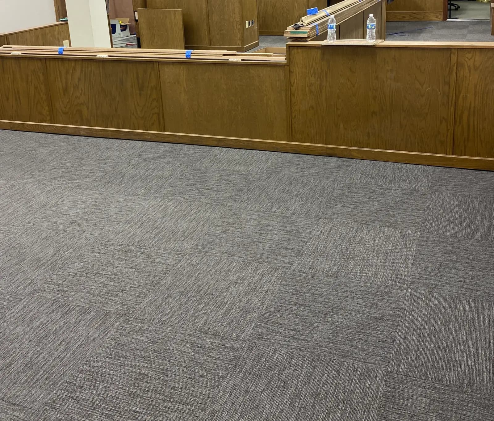 Grey commercial carpet tile laid quarter-turn across a courtroom floor at the DeSoto County Courthouse, oak jury-box millwork behind it