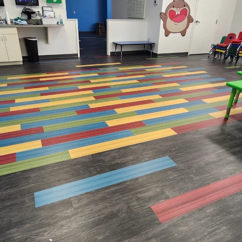 Detail of the four-color LVP accent rectangle scattered across dark wood-look luxury vinyl plank in the Heartland Church kids classroom