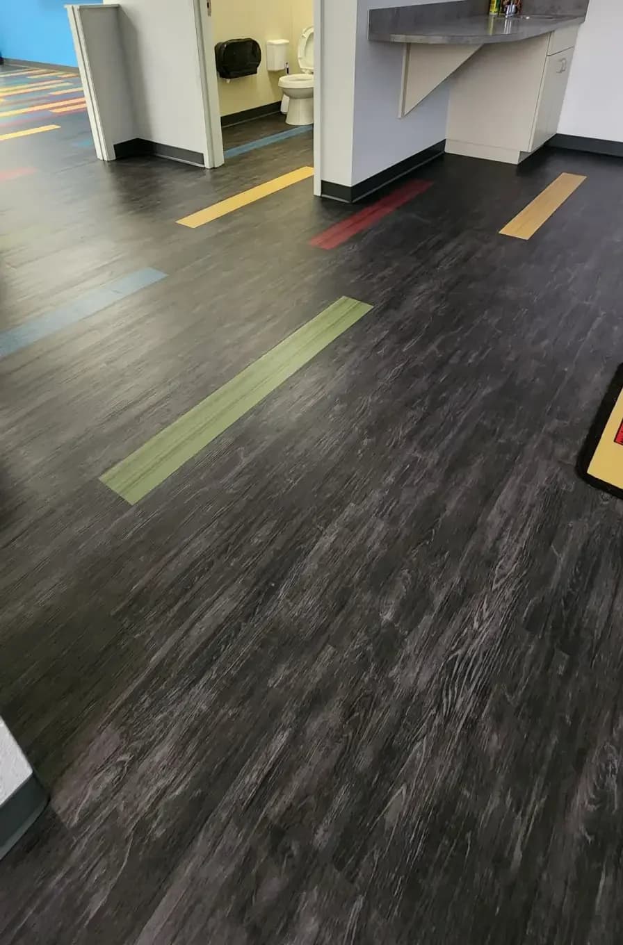 Dark wood-look commercial LVP running into the kids restroom hallway with single colored accent planks dropped in at random