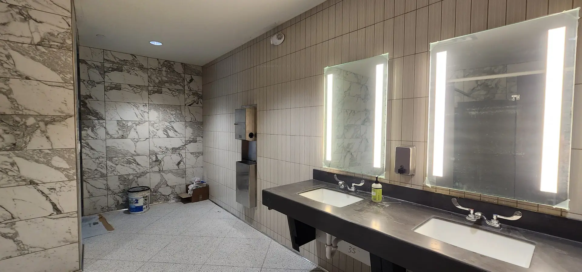 Wide view of the women's restroom with vertical ribbed accent tile, marble-look field tile, and speckled floor tile at Lake Ariana Civic Center