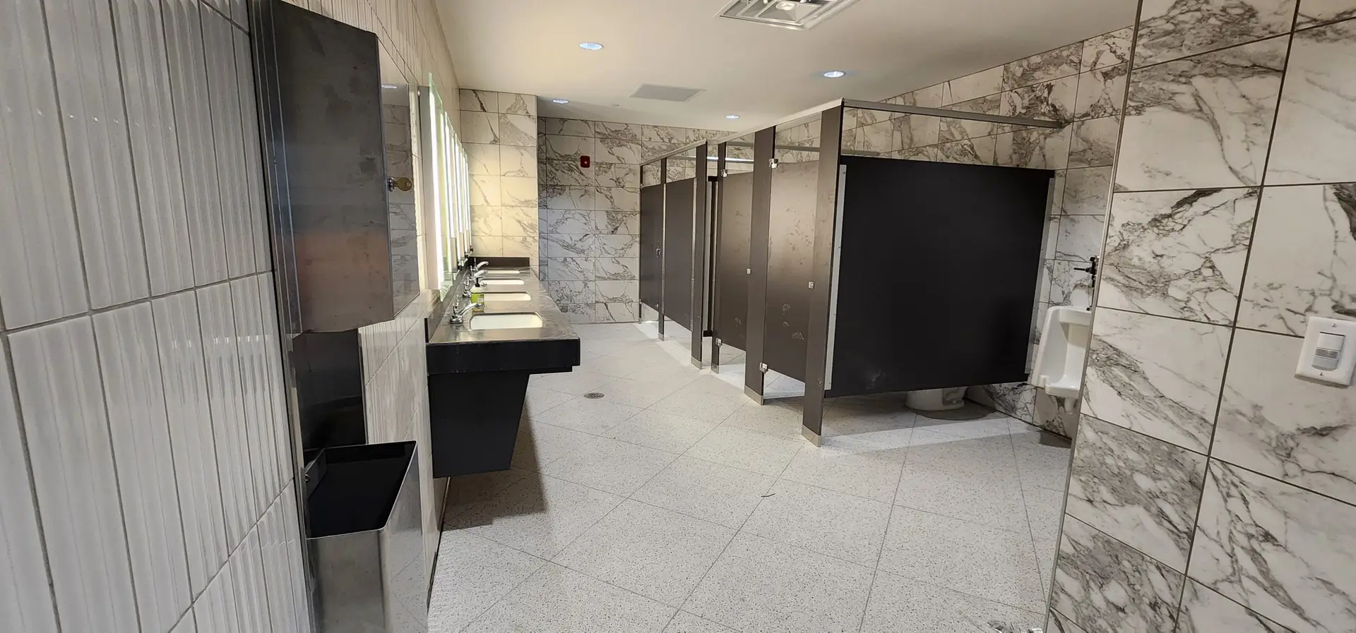 Restroom stalls flanked by marble-look porcelain wall tile and terrazzo floor tile at the Lake Ariana Civic Center, Auburndale, FL