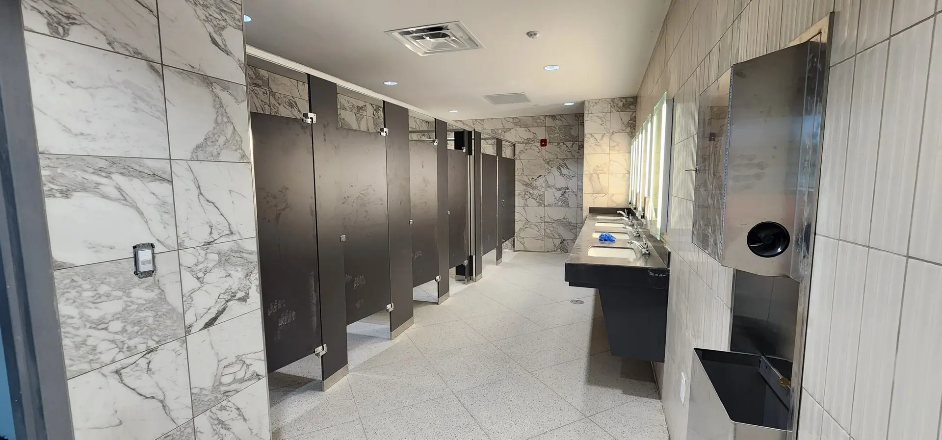 Looking down the restroom toward the marble-look tile accent wall and terrazzo floor at Lake Ariana Civic Center