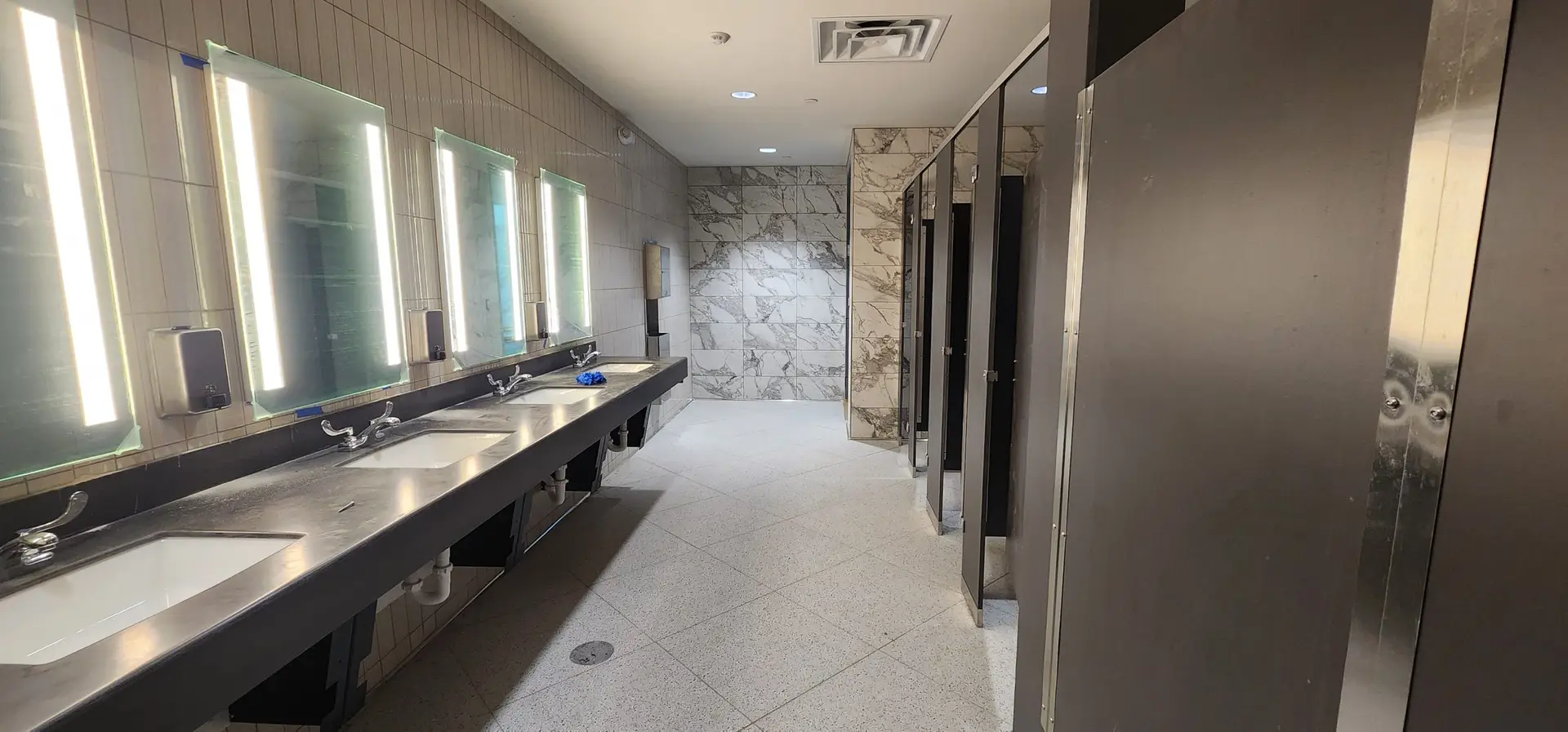 Vanity wall with backlit mirrors, ribbed white tile, and the marble-look accent wall in the Lake Ariana Civic Center restroom