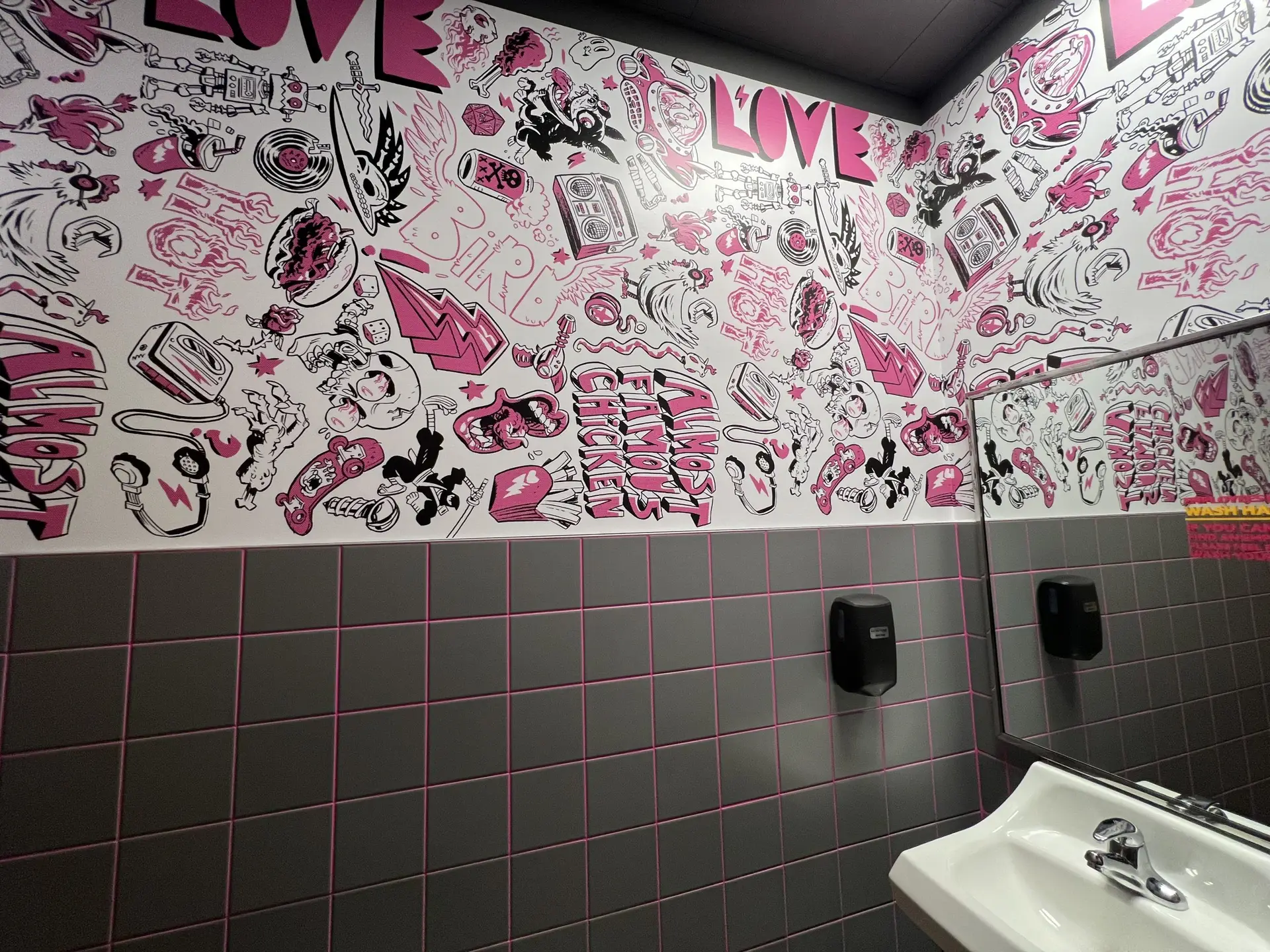 Gray wall tile with pink grout topped by the LoveBird Chicken pink and black graphic mural inside the restroom