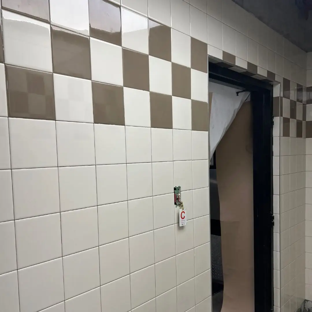 Corner detail of the tan and white Daltile checkerboard accent band wrapping the doorway in the Publix Fleet restroom