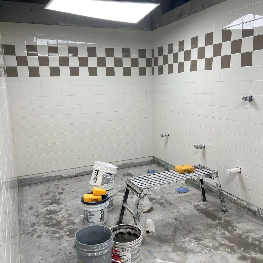 In-progress view of the Publix Fleet restroom with white wall tile and checkerboard accent set, concrete floor still pending finish