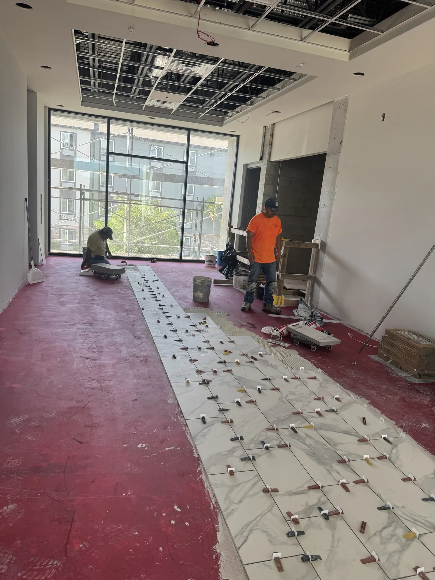 Installers we train and certify setting the first rows of common-area floor tile over the red waterproofing membrane at Sand Lake Vista
