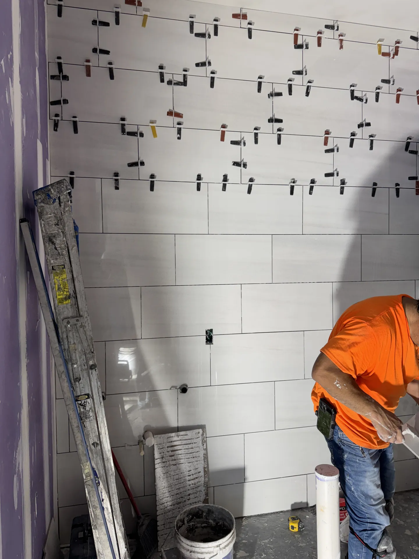 Installer setting 12x24 marble-look wall tile with leveling clips in a Sand Lake Vista office restroom