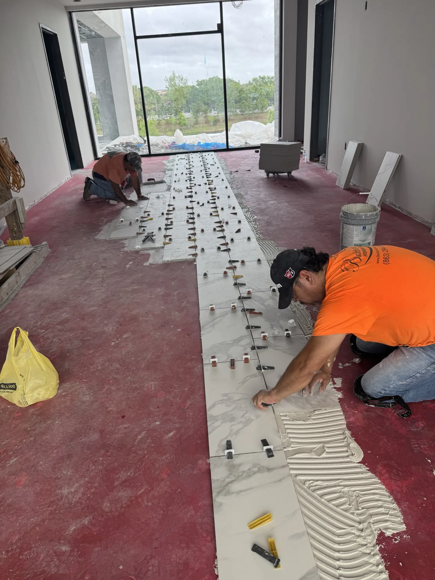 Installer troweling thinset and setting a run of marble-look porcelain floor tile toward the storefront windows at Sand Lake Vista in Orlando, FL