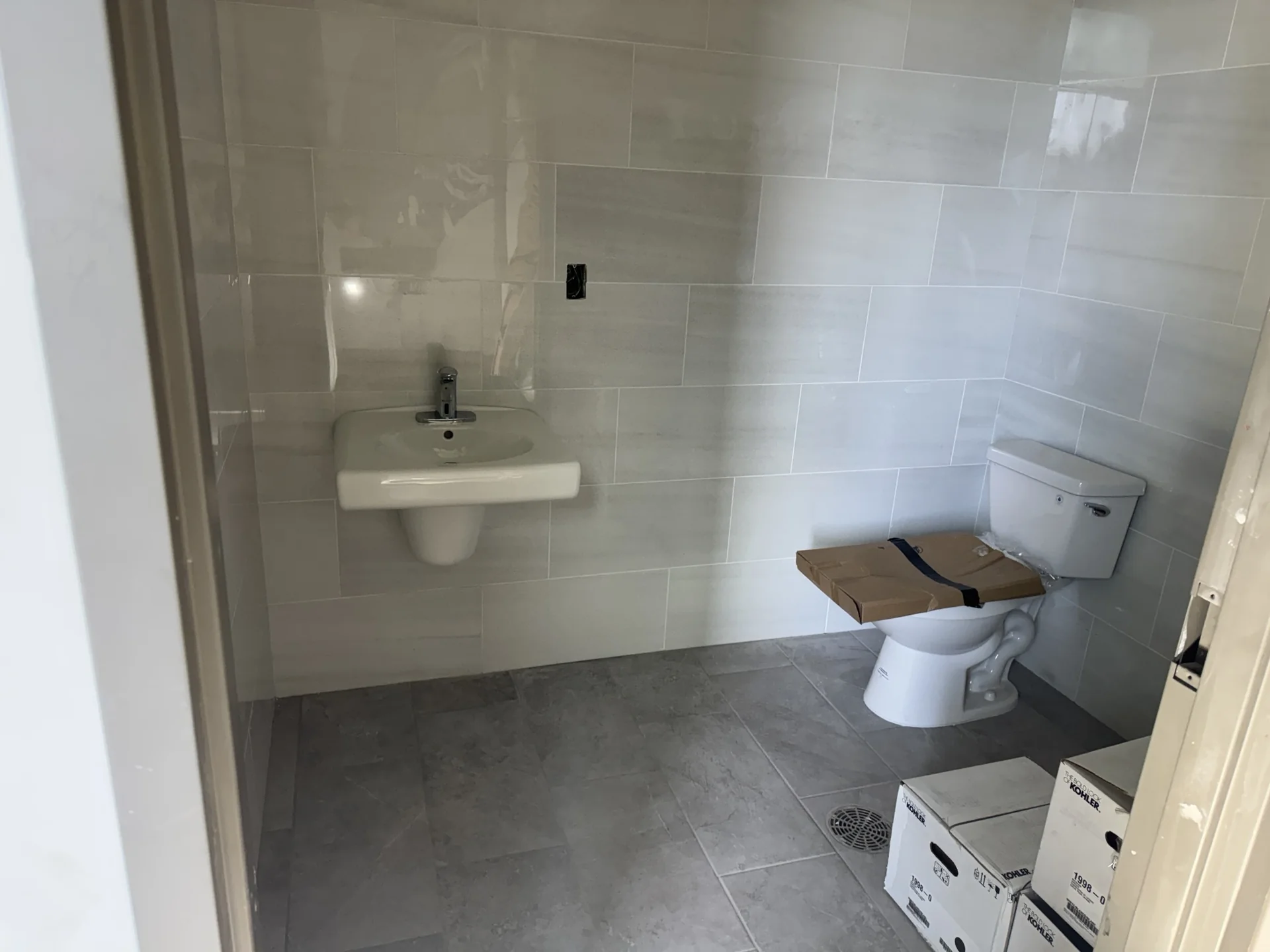 Finished office restroom at Sand Lake Vista in Orlando, FL with white marble-look porcelain wall tile and gray slip-resistant porcelain floor tile