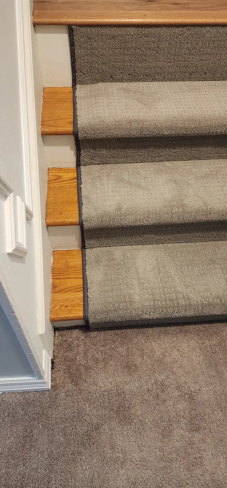 Top of the stairs where the gray runner meets wall-to-wall carpet on the landing, oak tread edges showing