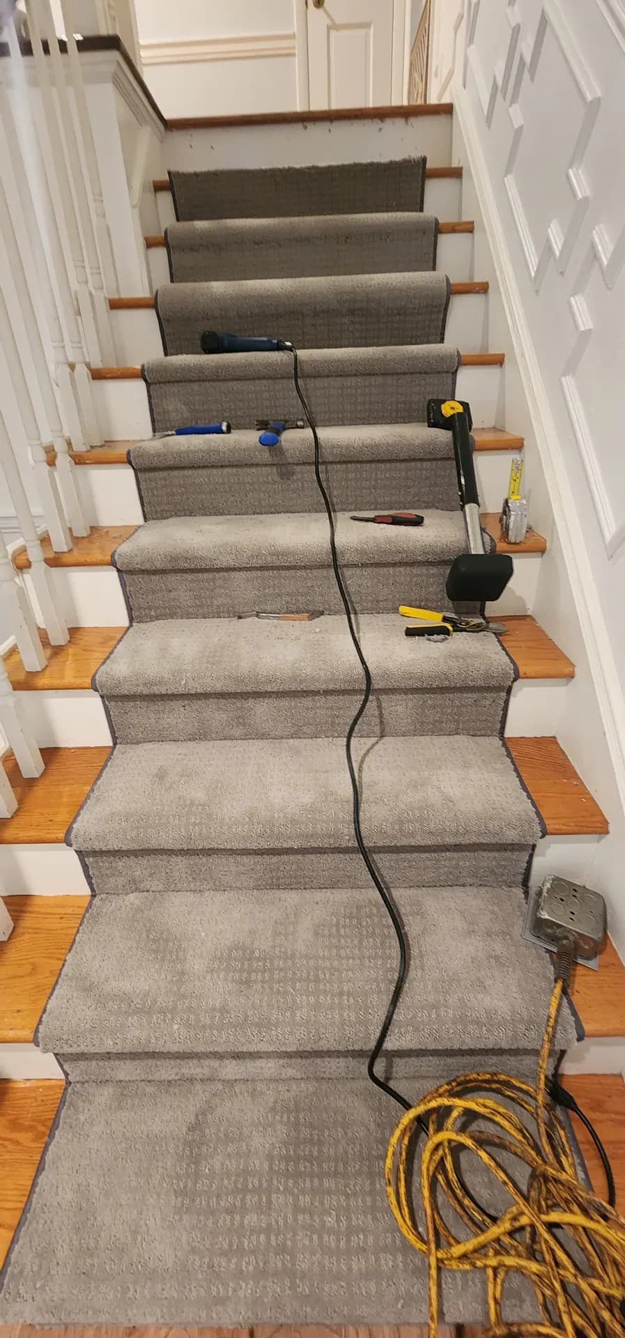 Runner installation in progress down a straight run of oak stairs, tools and a cord still on the treads