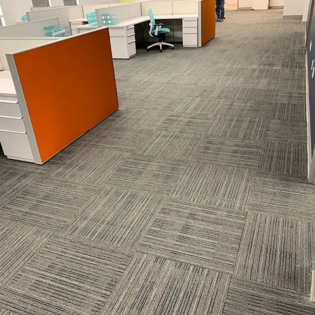 Gray patterned carpet tile in the Treatt USA open office workspace with orange and white cubicles